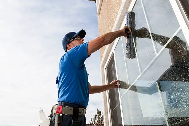 Window cleaning specialist inspecting glass edges and buildup with professional tools on tall home
